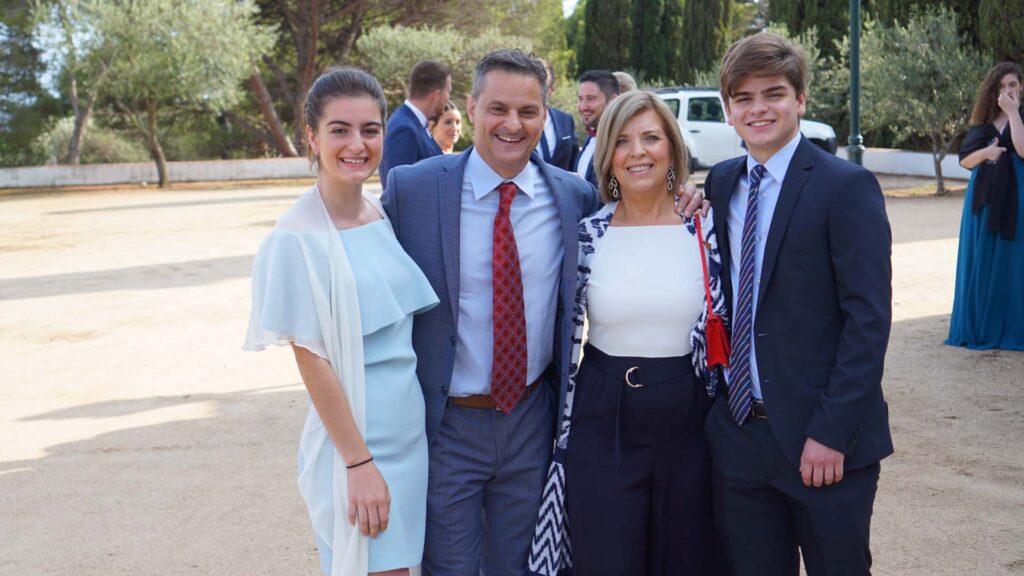 Victoria Puglia ’21 smiles alongside three family members in formal attire, outside. Trees can be seen in the distance.