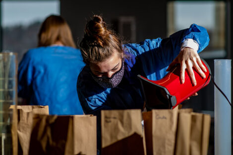 a student in a mask pours popcorn into paper brown bags