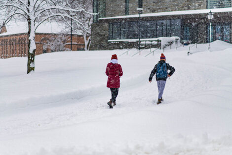 Two students walk away from the camera, toward Skillman Library, surrounded by snow