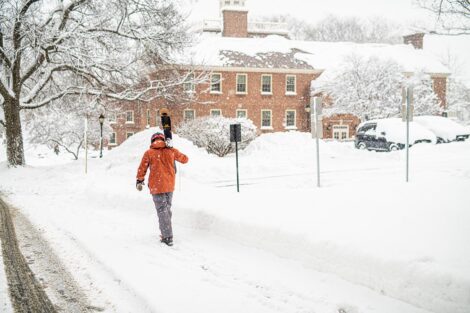Sebastian Wallach, facing away from the camera, walks along a snow-covered path, with skiis in his hand