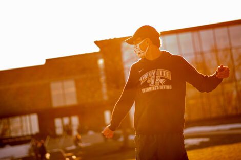 A masked student in a hat throws a frisbee outside of Skillman Library