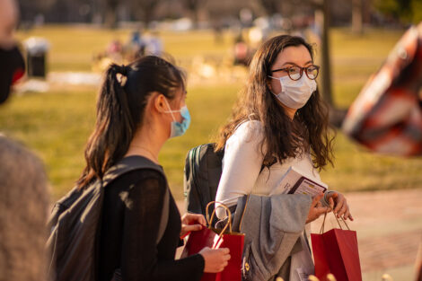 Two masked students carry red paper bags on the Quad.