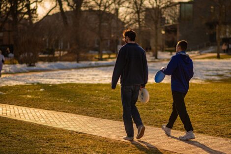 Two students walk down a path, holding frisbees.