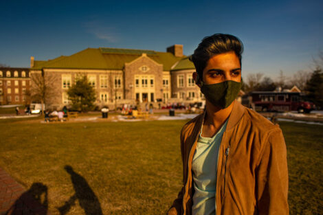A student wearing a mask in front of Farinon College Center on the Quad.