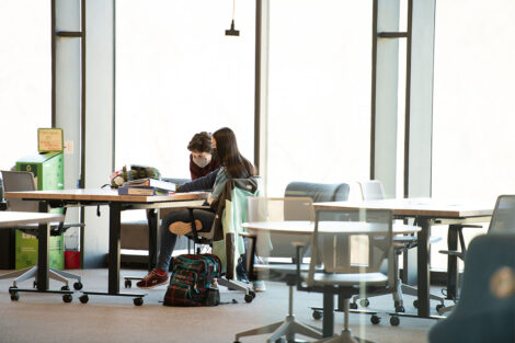 Masked students sit at tables in front of large windows at Rockwell Integrated Sciences Center