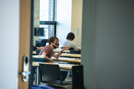 Masked students sit at tables inside of a classroom of Rockwell Integrated Sciences Center.