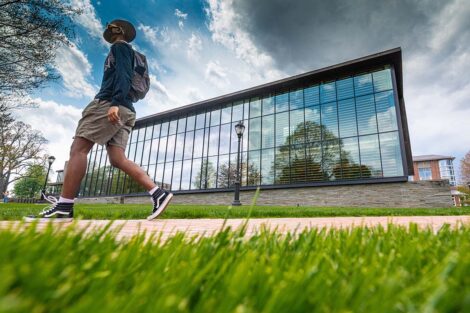 A student wearing a mask walks in front of Skillman Library