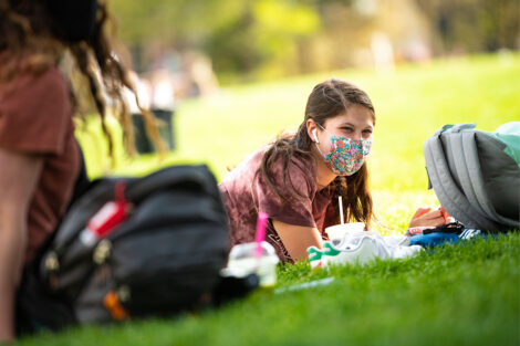 A masked student studies on the Quad.