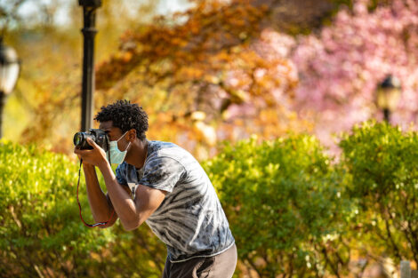 A masked student uses camera to take photos of campus.