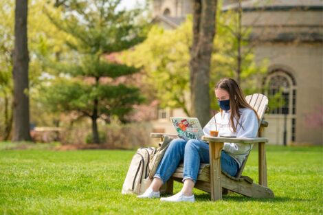 A masked student studies in an Adirondack chair.
