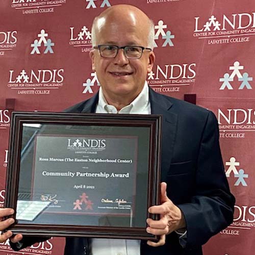 Ross Marcus holds a framed certificate in front of the Landis Center logo