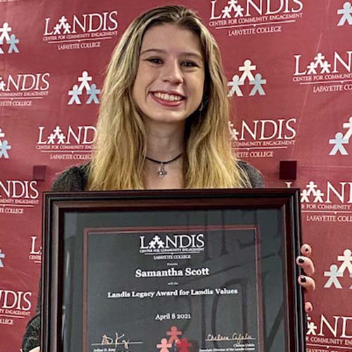 Sam Scott holds a framed certificate in front of the Landis Center logo