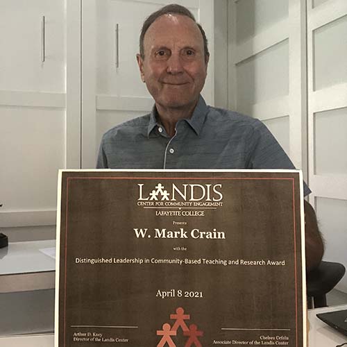 W. Mark Crain holds a framed certificate in front of the Landis Center logo
