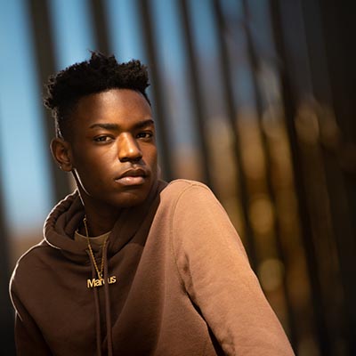 Light captures a serious look on student's face with his one shoulder forward and the other shoulder back in the shadows toward Skillman library