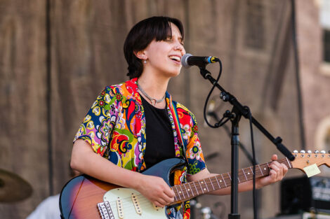 guitar player sings into a mic on a stage on the Quad