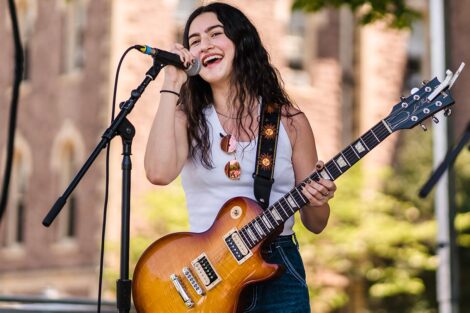 guitar player sings into a mic on a stage on the Quad