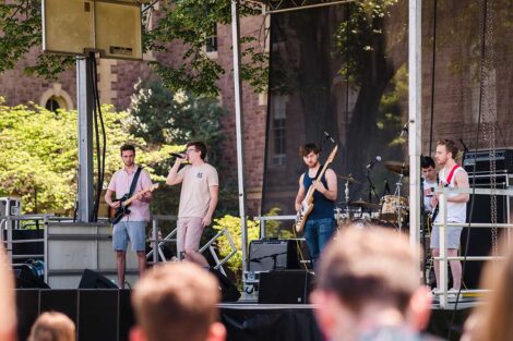 students sing and play guitar in band on a stage on the Quad