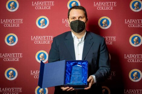 Joshua Smith holding Aaron O. Hoff Award and standing in front of Lafayette College backdrop