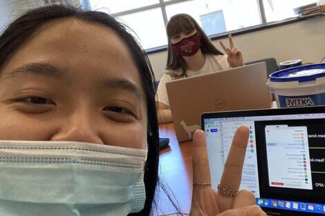 Two students at laptops flash the peace sign