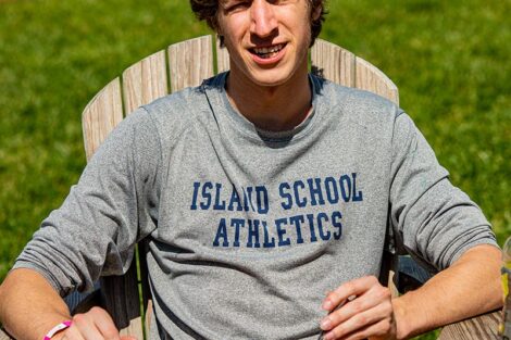 A student sits on an Adirondack chair, eating a pizza.