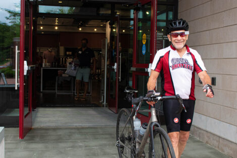 man in Lafayette cycling gear leaves College store walking with bike