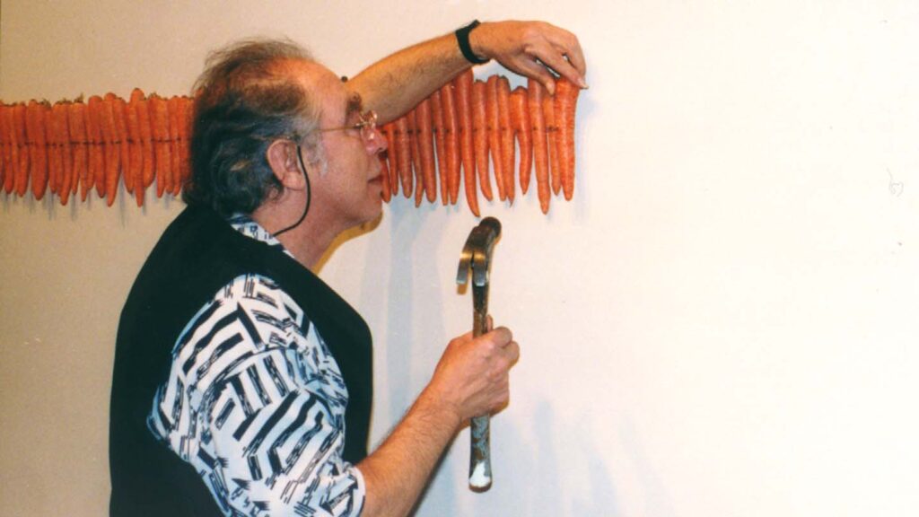 Artist holding hammer nails carrots to the wall