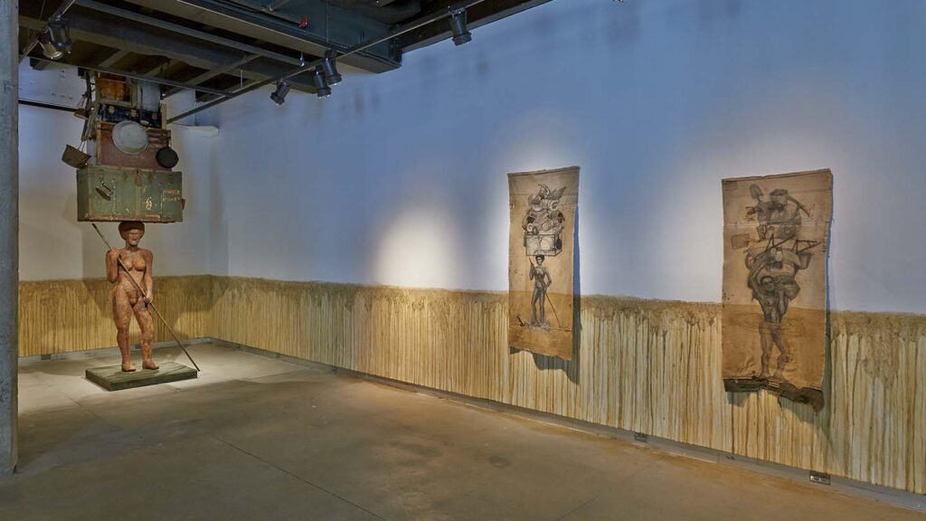 Mud marks the walls in the gallery around a hanging works and a statue on the floor