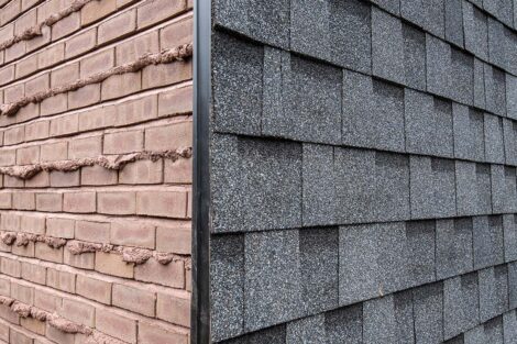 Corner of house with shingles on one angle and brown brick with weeping joints on the other side