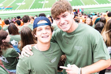 students in matching green Tshirts smile, Fisher Field in background