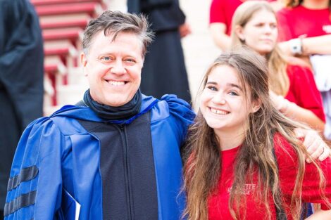 Professor Jim Dearworth wears robe, stands with daughter in red Tshirt smile