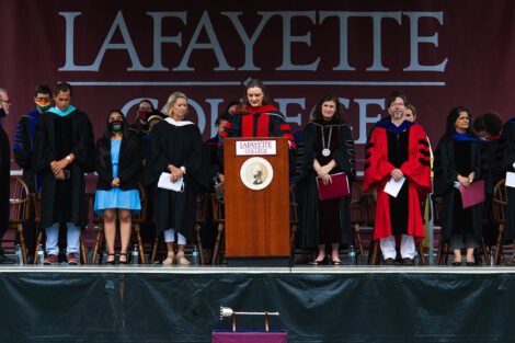 chaplain Alex Henderickson stands at podium, podium dignitaries surround her