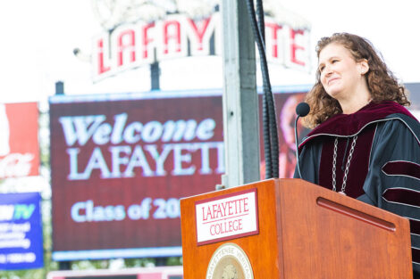 President Nicole Hurd smiles at podium, Fisher Field jumbo-tron says