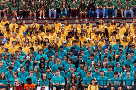 students fill the stands at Fisher Field, they sit in groups with matching red, bule, and green Tshirts