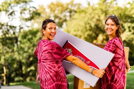 two students in Welcome home tie-dye shirts smile outdoors