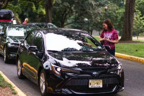 President Hurd wears Welcome Home T-shirt and talks to people in a car driving on campus