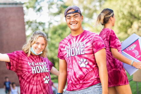 two students in Welcome home tie-dye shirts smile outdoors