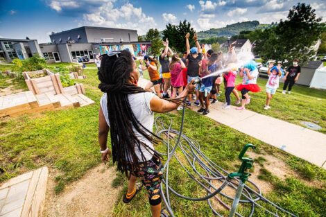 A person sprays a garden house at a group of students and children from the Boys and Girls Club.