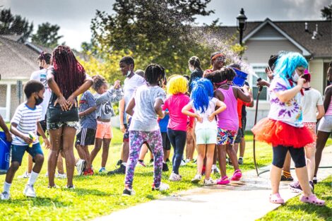 Children from the community and Lafayette students are sprayed with a water hose outside.
