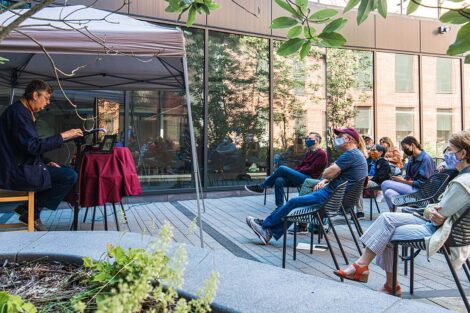 Families sit outside at Goodwyn Plaza, Rockwell Integrated Science Center, listening to John Becica ’69