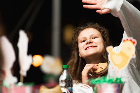 A student waves, holding ice cream while sitting at a table.