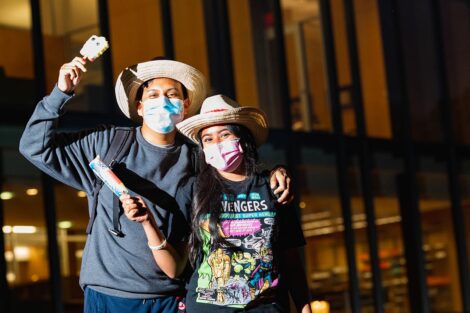 Two masked students hold ice cream bars, wearing matching cowboy hats.