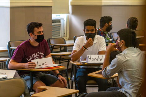 Students, wearing masks, sit at desks in a semi-circle, inside a classroom at Lafayette College.
