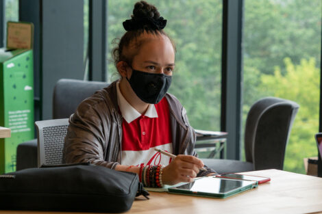 A student, wearing a mask, uses their tablet.