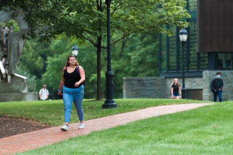 A student walks along a brick pathway in front of Lafayette College's Skillman Library. A portion of the sculpture Transcendence can be seen.