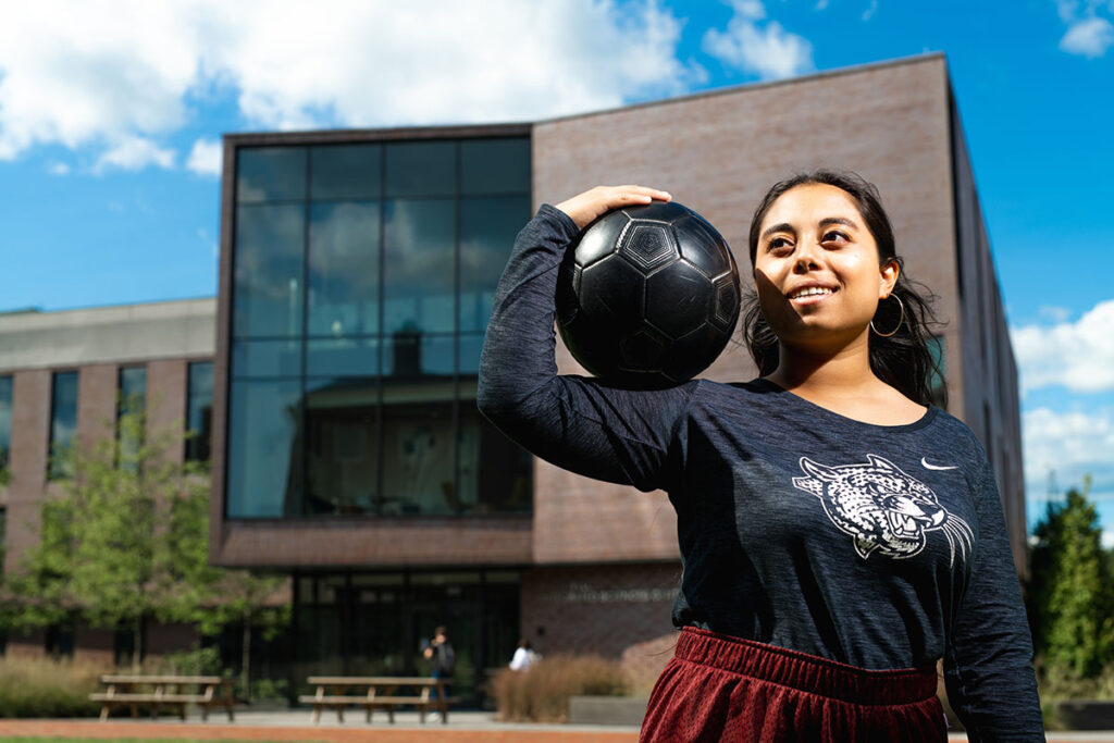 Flor De Maria Caceres Godoy holds a soccer ball outside of Rockwell Integrated Sciences Center