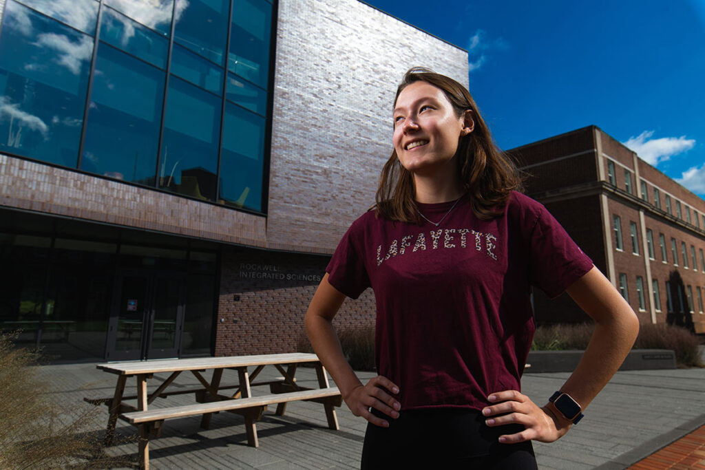 Maddie Carroll smiles with hands on hips in front of Rockwell Integrated Sciences Center.
