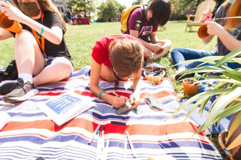 students in masks sit on blankets on the Quad and write messages