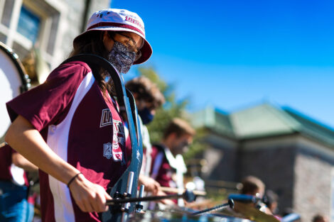 Masked student plays the drums in front of Hogg Hall.