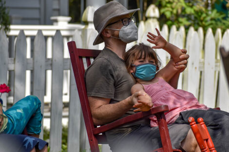 masked parent holds young masked child on rocking chair