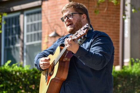 person plays guitar and sings in front of house